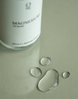 Foto van onze magnesiumspray naast een paar druppels magnesiumolie. Hoogwaardige magnesiumsuppletie voor huidtoepassing, ontspanning, spierherstel, verbeterde slaap, gezonde botten en hartgezondheid. Gemakkelijk online te bestellen via onze webshop.
