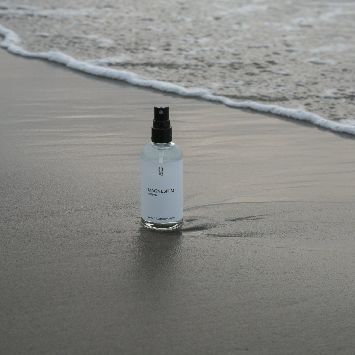 100ml fles magnesiumolie op het zand bij het strand. Ondersteunt dagelijkse magnesiumsuppletie, ontspanning, spierherstel, een gezonde slaap en het behoud van bot- en hartgezondheid. Verkrijgbaar in onze magnesium webshop.