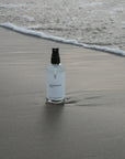 100ml fles magnesiumolie op het zand bij het strand. Ondersteunt dagelijkse magnesiumsuppletie, ontspanning, spierherstel, een gezonde slaap en het behoud van bot- en hartgezondheid. Verkrijgbaar in onze magnesium webshop.