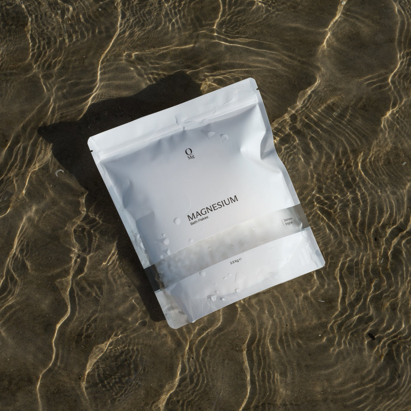 Foto van de verpakking van onze magnesiumcapsules die op het strand ligt, omringd door water. Ideaal voor dagelijkse magnesium suppletie ter ondersteuning van spierontspanning, welzijn en een gezonde magnesiumbalans. Verkrijgbaar in onze webshop.