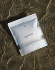 Foto van de verpakking van onze magnesiumcapsules die op het strand ligt, omringd door water. Ideaal voor dagelijkse magnesium suppletie ter ondersteuning van spierontspanning, welzijn en een gezonde magnesiumbalans. Verkrijgbaar in onze webshop.