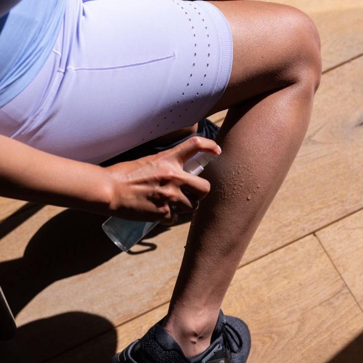 Female in a blue outfit spraying magnesium oil on calves.