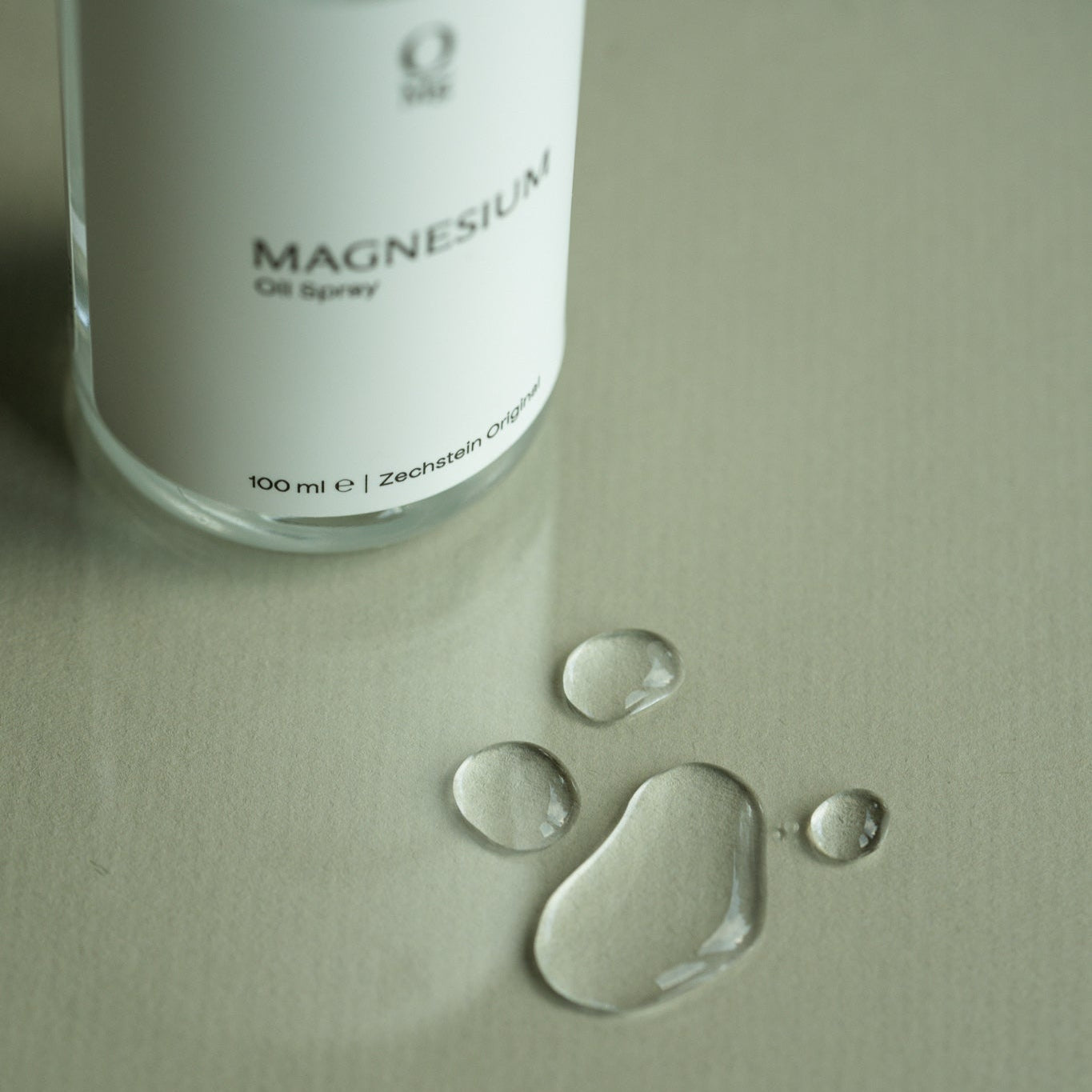 Foto van onze magnesiumspray naast een paar druppels magnesiumolie. Hoogwaardige magnesiumsuppletie voor huidtoepassing, ontspanning, spierherstel, verbeterde slaap, gezonde botten en hartgezondheid. Gemakkelijk online te bestellen via onze webshop.