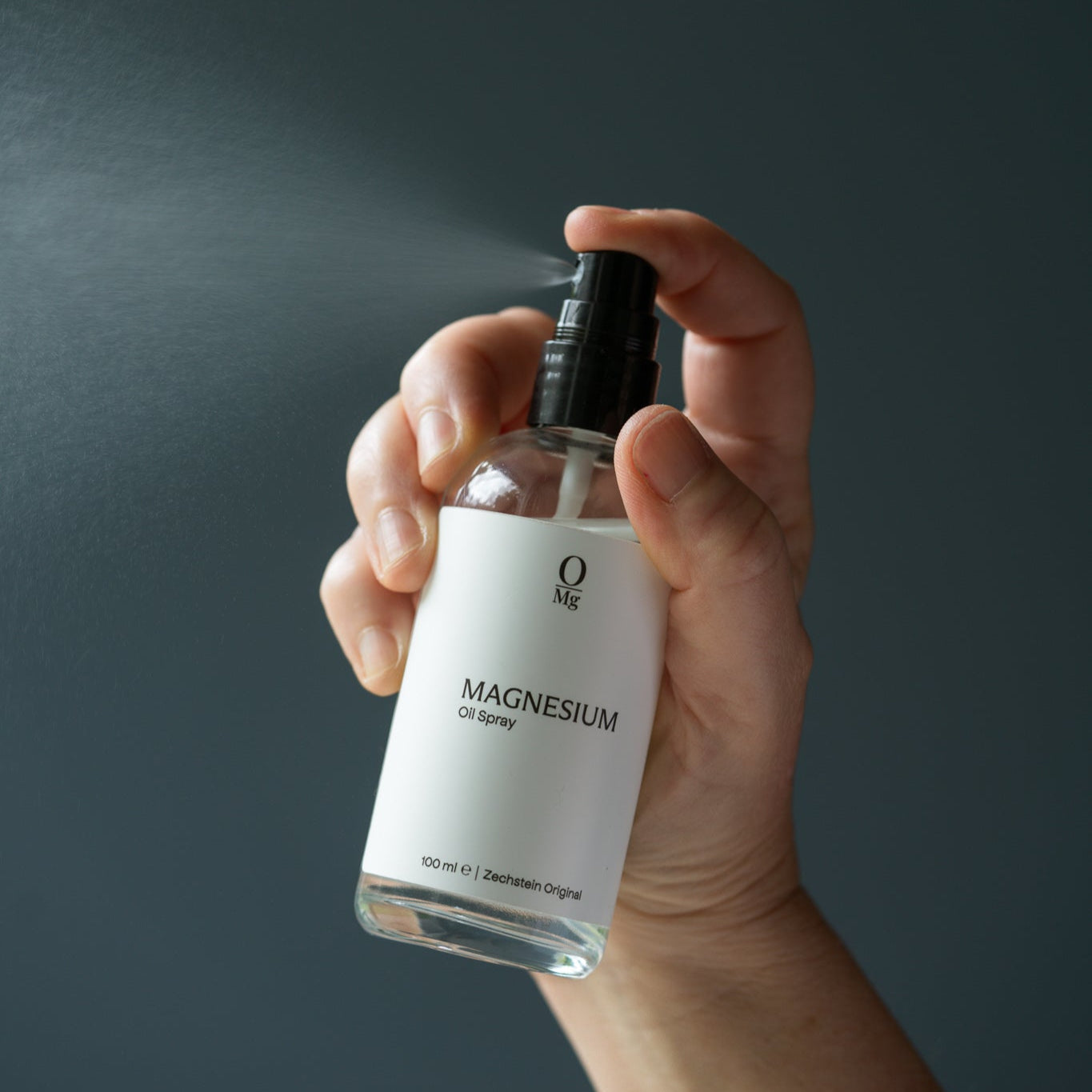 Hand houdt een flesje magnesiumspray vast terwijl er spray uit komt. Ondersteunt huidtoepassing van magnesium, ontspanning van spieren, spierherstel, betere slaap en een gezonde magnesiumbalans. Verkrijgbaar in onze magnesium webshop.