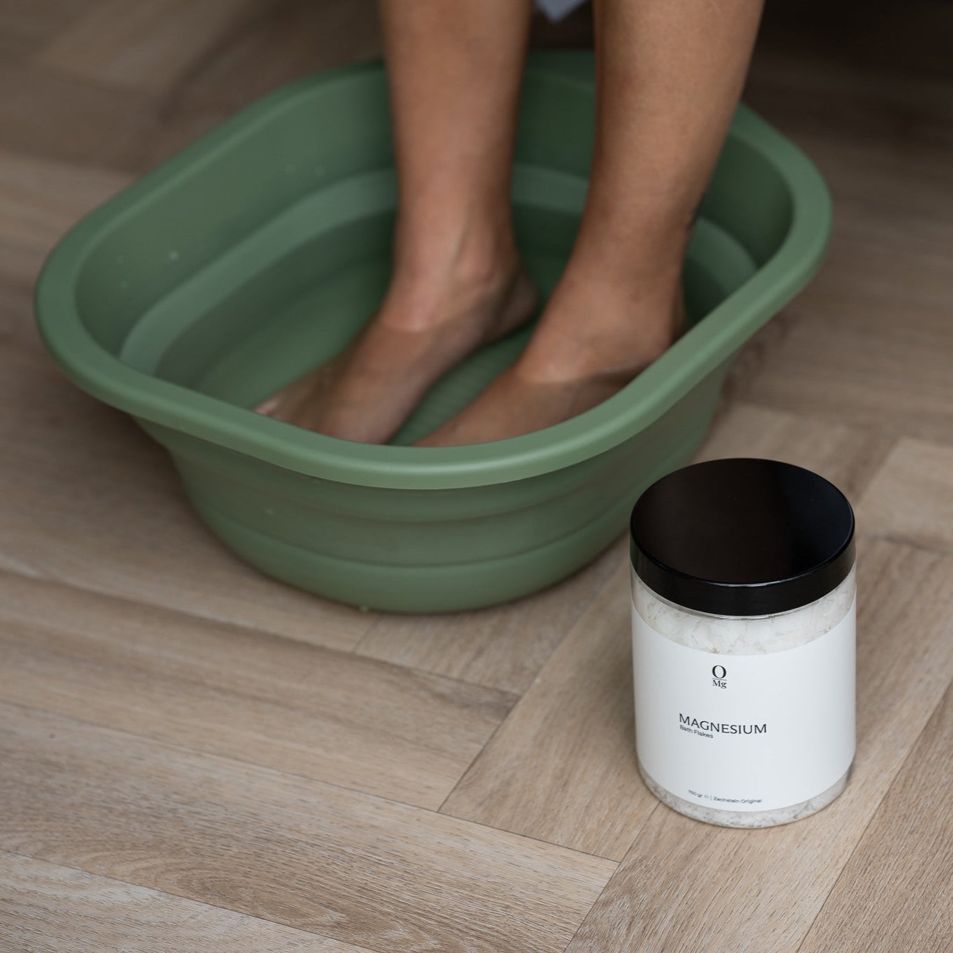 Foto van iemand die ontspant in een magnesium voetenbad, met daarnaast de verpakking van 750 gram magnesiumvlokken. Ideaal voor spierontspanning, ontspanning en ondersteuning van de dagelijkse magnesiumbalans. Gemakkelijk te bestellen via onze webshop.
