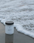 Foto van onze magnesiumpot geplaatst in de branding op het strand. Ondersteunt diepe slaap, ontspanning van spieren, gezonde stressniveaus, stabiele bloedsuikers, hart- en botgezondheid en kan helpen bij PMS en hormonale balans. Gemakkelijk te bestellen via onze webshop.
