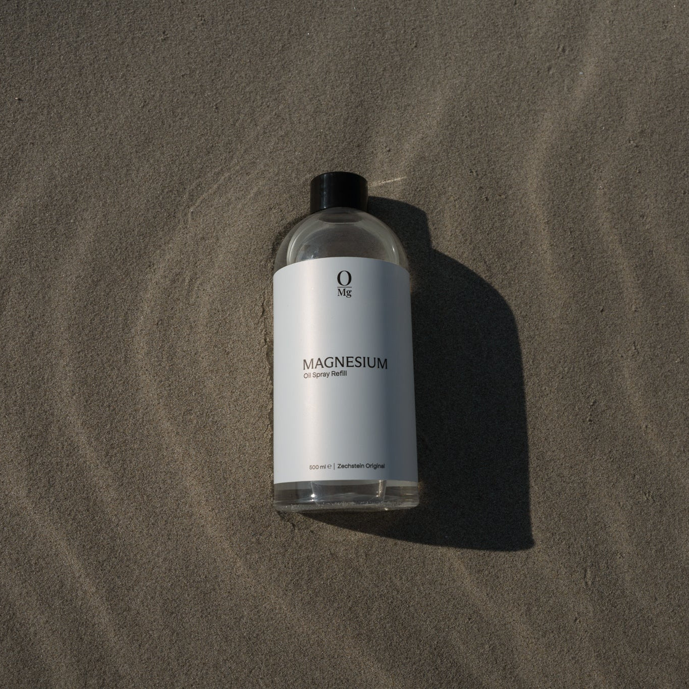 500ml navulfles magnesiumolie liggend op het strand, sfeervol gepresenteerd voor een gevoel van ontspanning en wellness. Verkrijgbaar in onze webshop voor dagelijks gebruik en eenvoudig navullen.