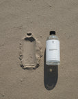 Foto van een 500ml navulfles magnesiumolie die op het strand ligt. Deze magnesium olie is goed voor ontspanning, huidverzorging en spierherstel, en eenvoudig te bestellen via onze webshop.